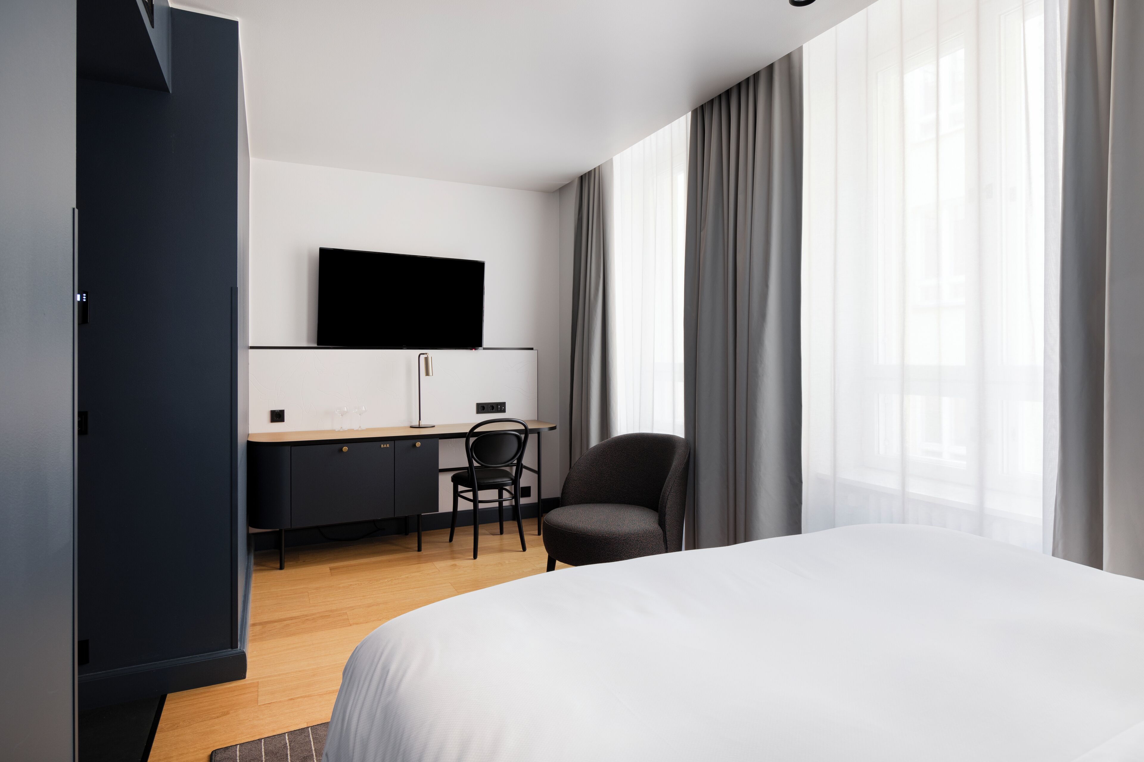 Moderni hotellihuone, jossa on sänky, työpöytä tuolilla, taulutelevisio ja vaatekaappi.