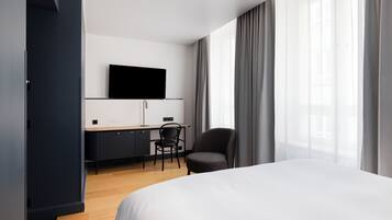 Moderni hotellihuone, jossa on sänky, työpöytä tuolilla, taulutelevisio ja vaatekaappi.