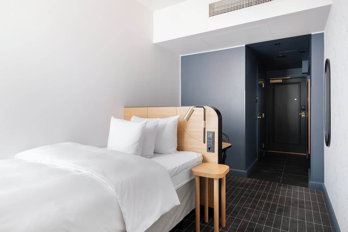 Una habitación de hotel moderna con una cama, una mesita de noche y una puerta que da a otra habitación.
