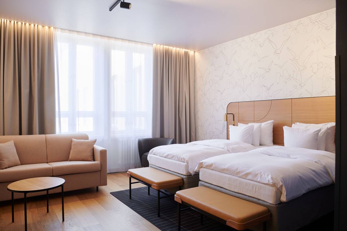 Una habitación de hotel con un sofá, dos camas, una mesita y una silla.