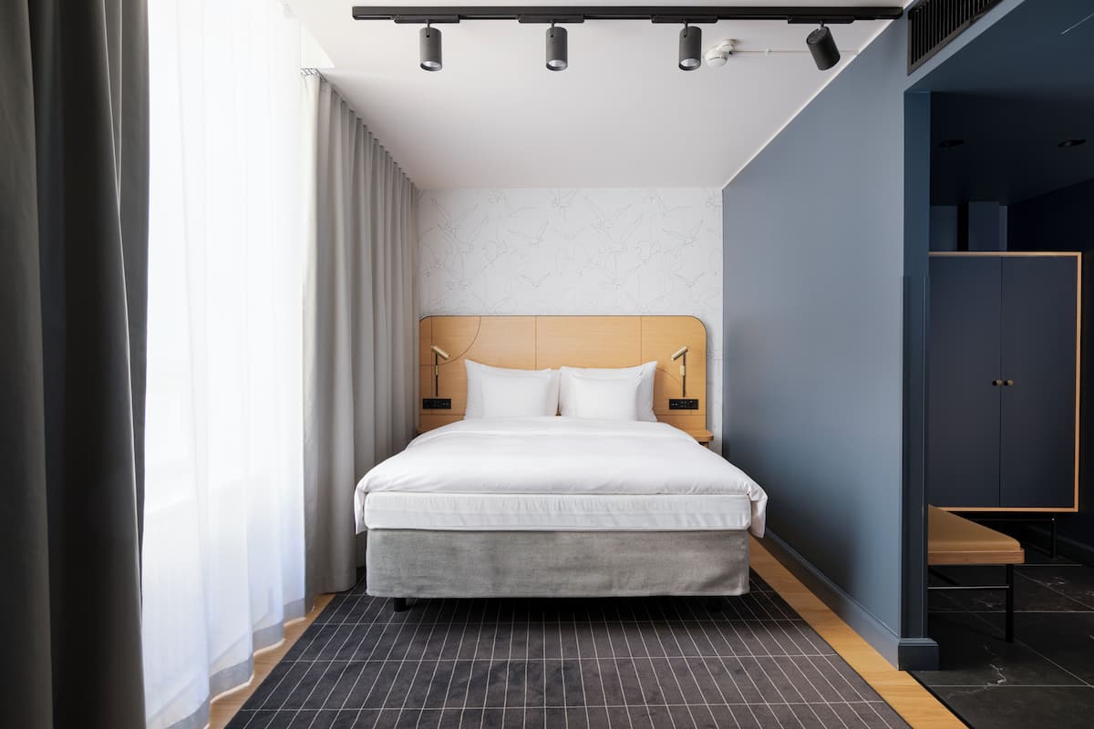 Habitación de hotel moderna con una cama grande, cabecera de madera y vista a la ciudad por la ventana.