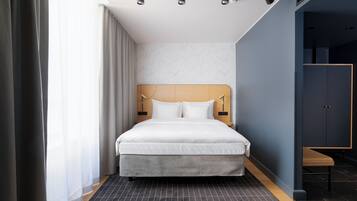 A modern hotel room with a large bed, a wooden headboard, and a view of the city through the window.