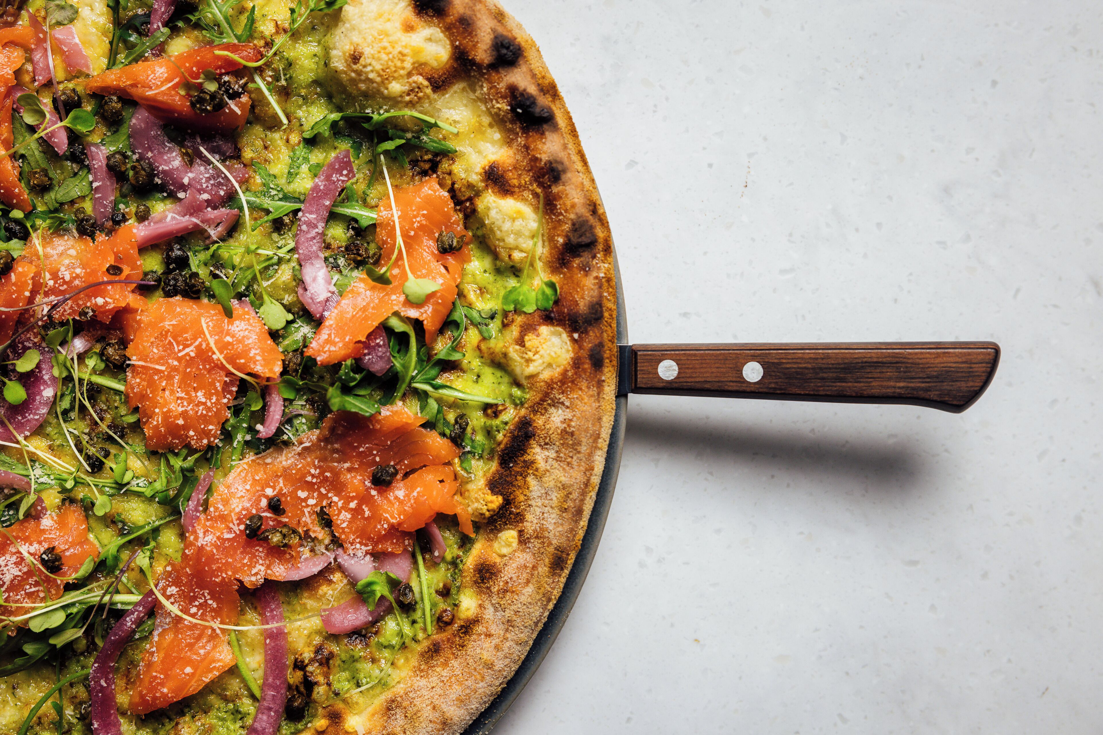 Una pizza con varios ingredientes sobre una pala de madera.