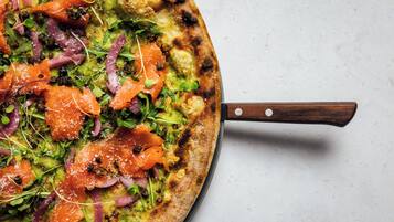 Una pizza con varios ingredientes sobre una pala de madera.