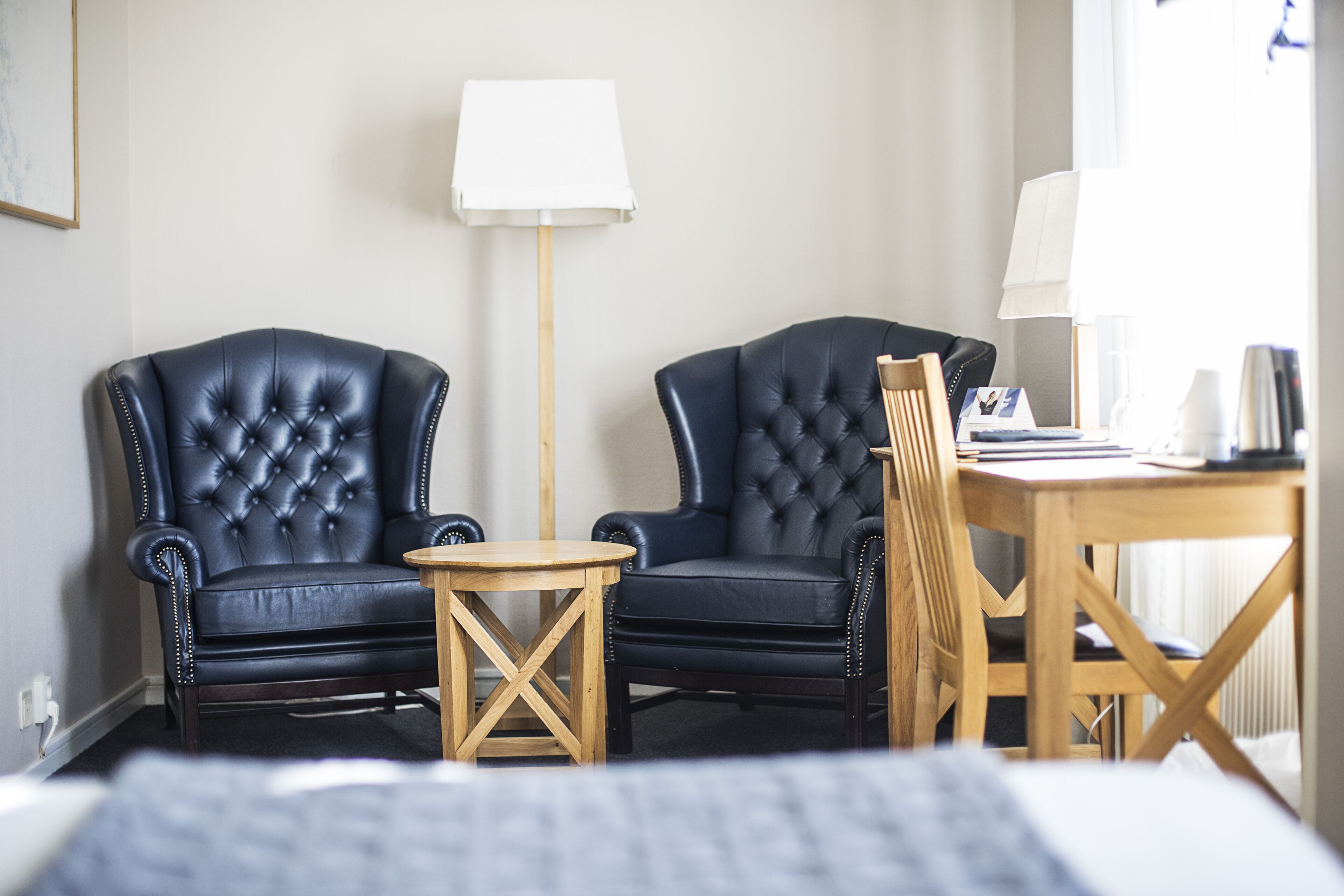 Hotellihuone, jossa on kaksi mustaa nahkaista nojatuolia, puinen sivupöytä, puinen ruokapöytä tuoleineen ja lamppu.