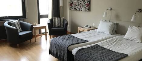 Habitación de hotel con dos camas, un escritorio, una silla, un tapete rojo y una ventana con cortinas.