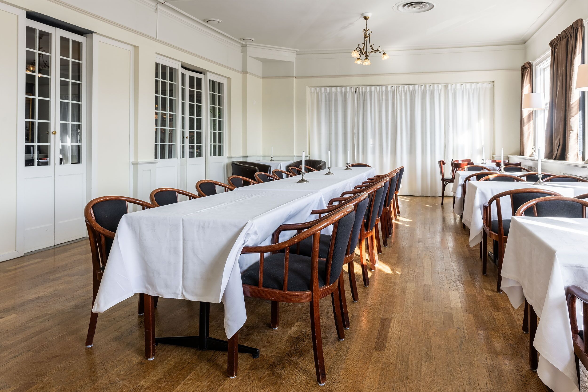 Un comedor con una larga mesa dispuesta para una comida, rodeada de sillas de madera con asientos acolchados.