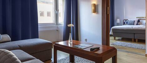 A modern hotel room with a sofa, a wooden table, and a view of the city through a window.