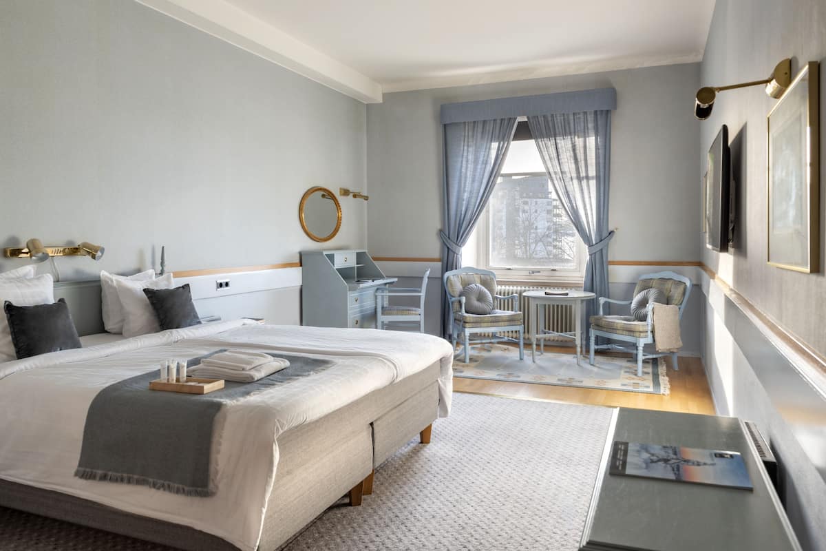 A hotel room with a large bed, a desk, a chair, and a window with curtains.