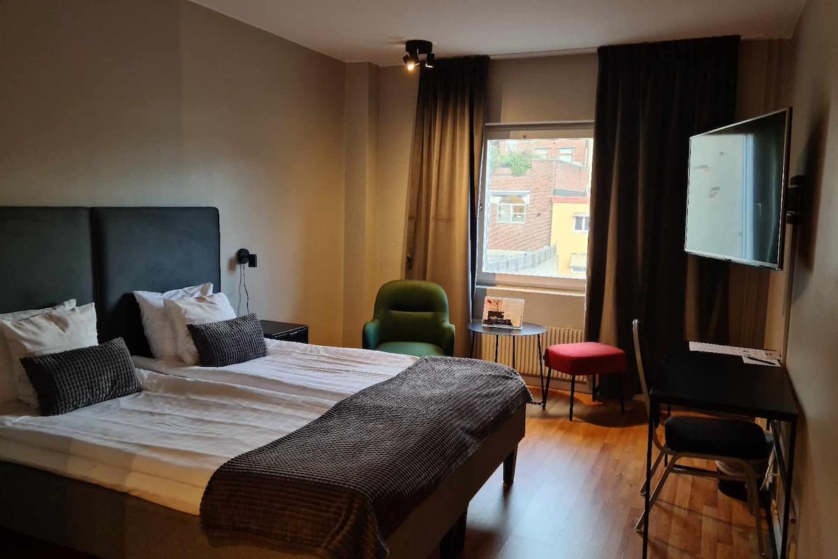 A hotel room with a large bed, a desk, a chair, and a TV.