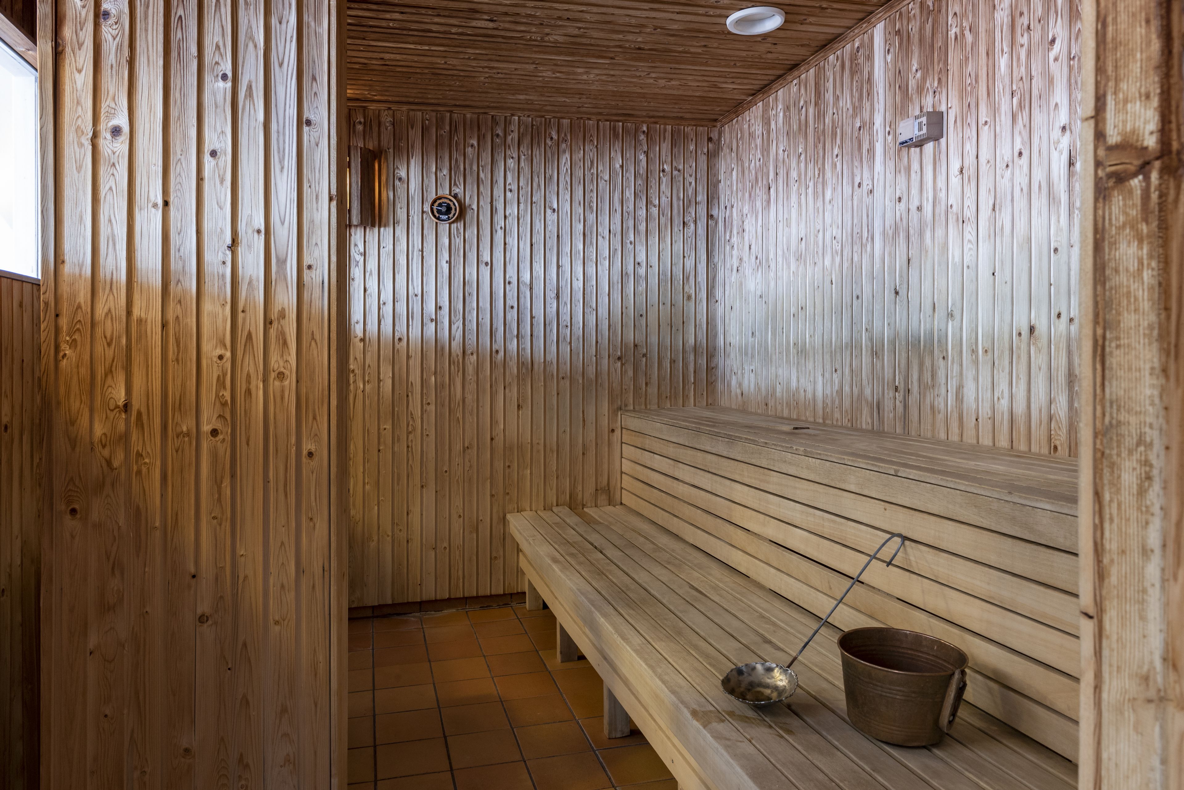 Eine Sauna mit Holzwänden und -bänken, einem gefliesten Boden und einem Eimer auf einer der Bänke.