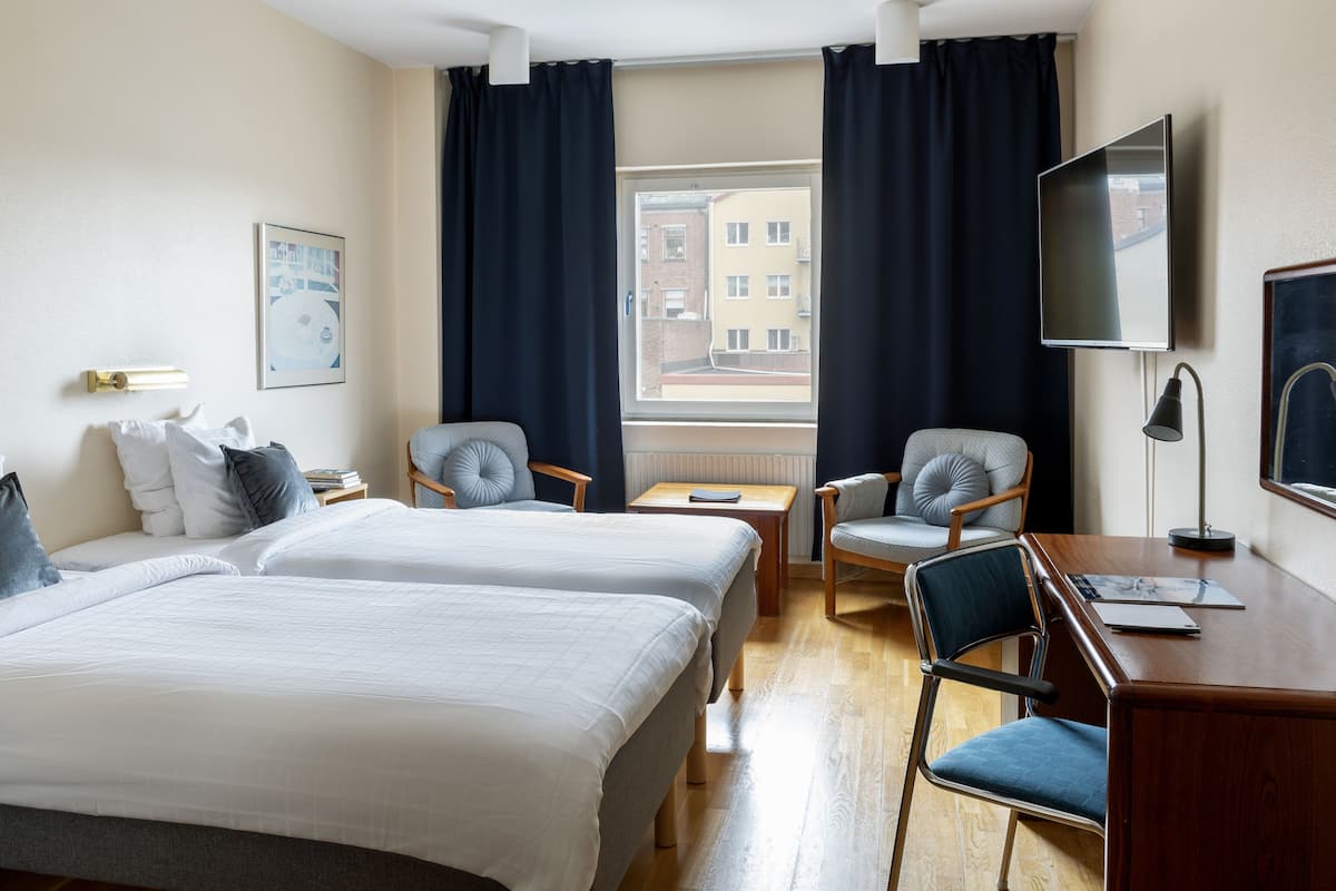 A hotel room with two beds, a desk, a chair, a TV, and a window with curtains.
