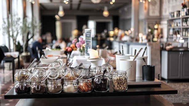 A buffet table with various food items in jars and containers, a candle centerpiece, and a bar area in the background. - First Hotel Statt Örnsköldsvik (Ornskoldsvik)
