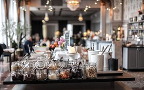 A buffet table with various food items in jars and containers, a candle centerpiece, and a bar area in the background. - First Hotel Statt Örnsköldsvik (Ornskoldsvik)