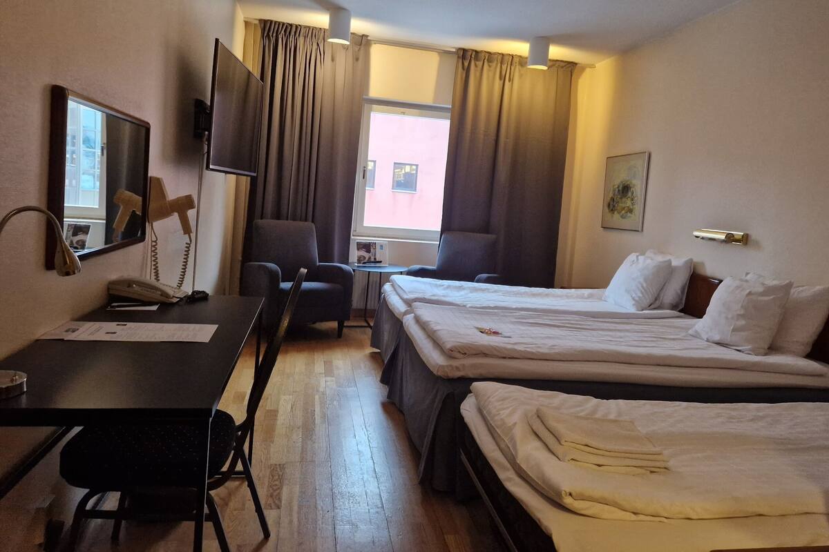 A hotel room with two beds, a desk, a chair, a TV, and a window with curtains.