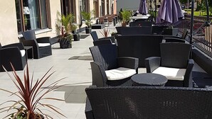 An outdoor seating area with wicker furniture and umbrellas, a building with arched windows, and potted plants. - First Hotel Statt Örnsköldsvik (Ornskoldsvik)