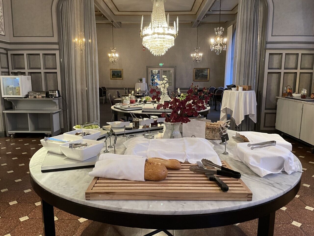 A dining area with a round table set for a meal, featuring bread, utensils, and a vase with flowers.