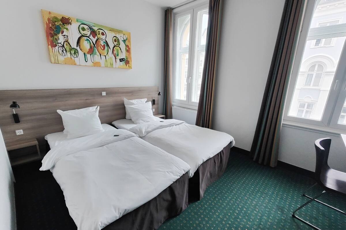 Habitación de hotel con dos camas, alfombra verde, un cuadro en la pared y una ventana con cortinas.