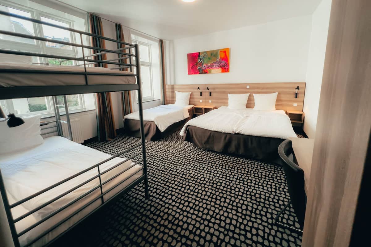 Habitación de hotel con literas, una cama individual, cabecero de madera, un cuadro y suelo estampado.
