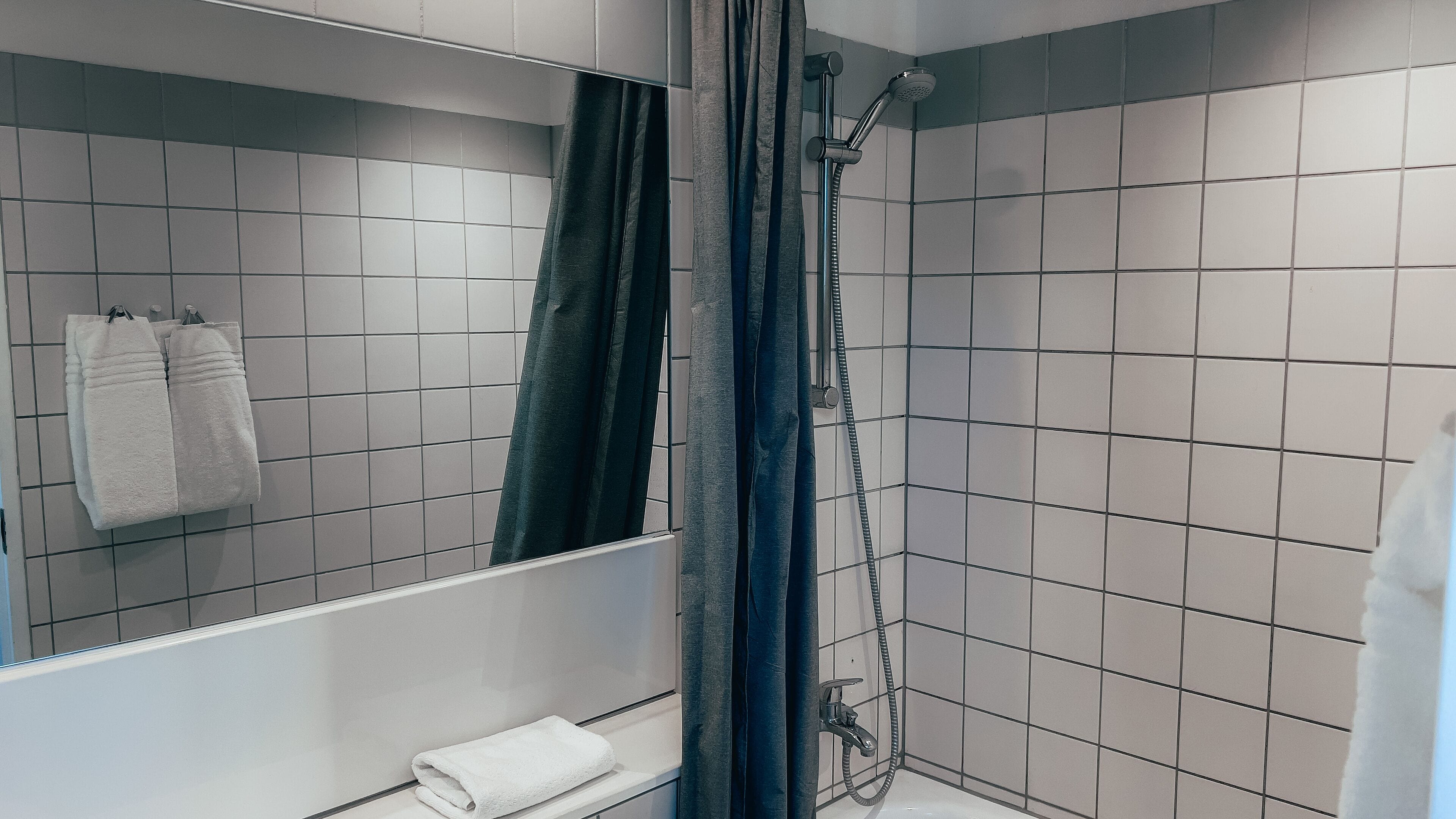 A modern bathroom with white tiles, a shower, and a mirror.