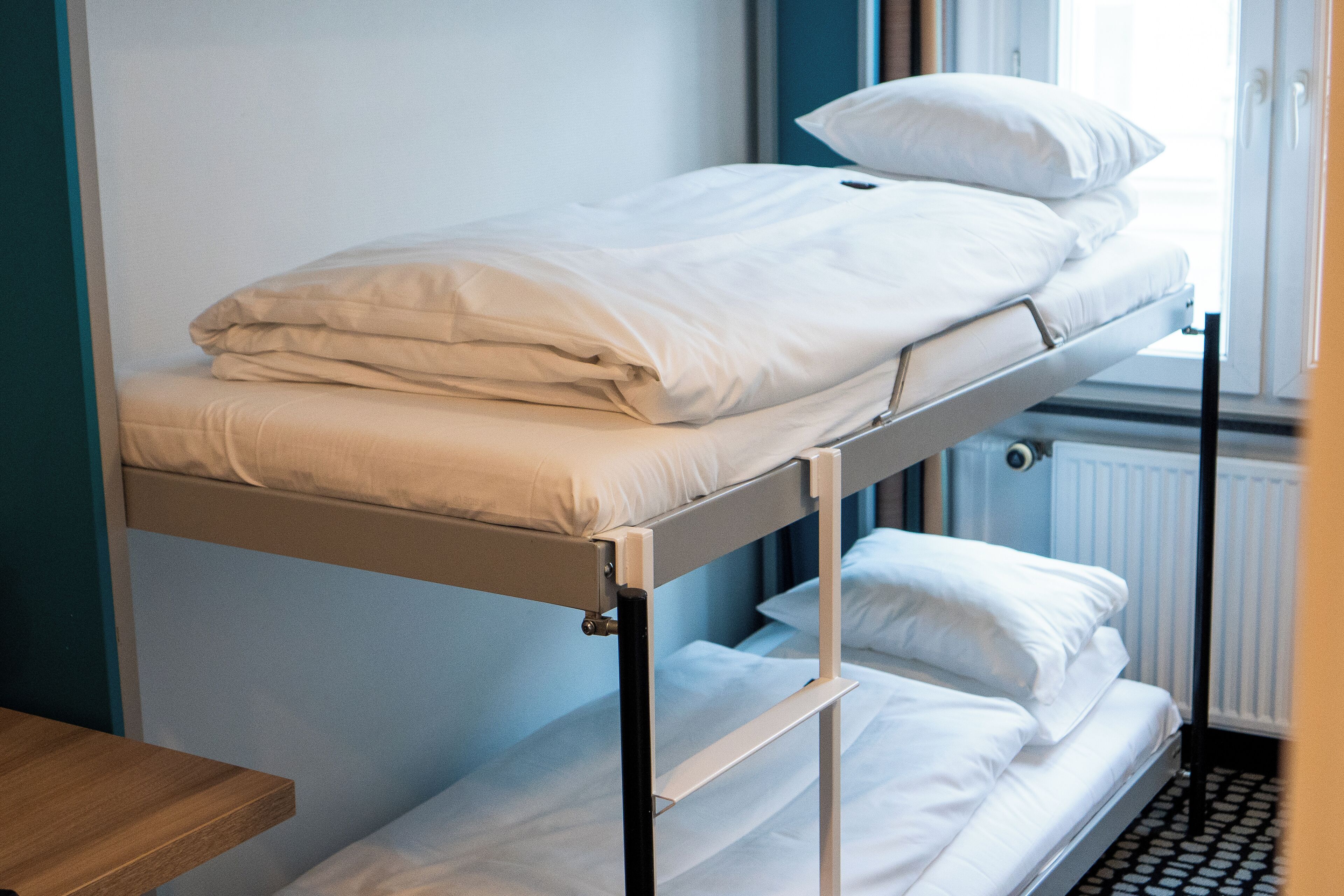 A bunk bed with white bedding and a wooden nightstand.