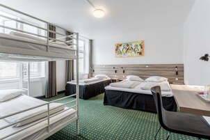 A dormitory room with bunk beds, a desk, a chair, and a painting on the wall.