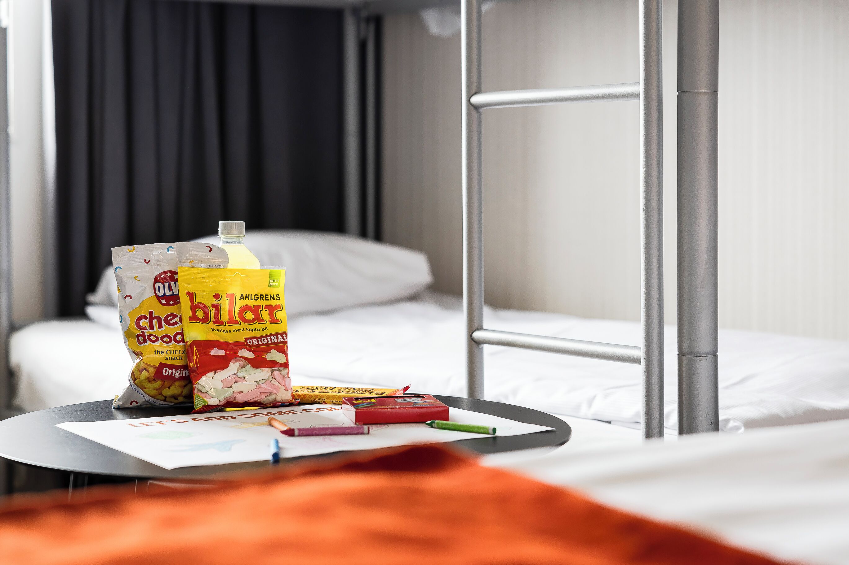 Ein Hotelzimmer mit Etagenbett, Nachttisch mit Snacks, Saftflasche und Notizbuch.