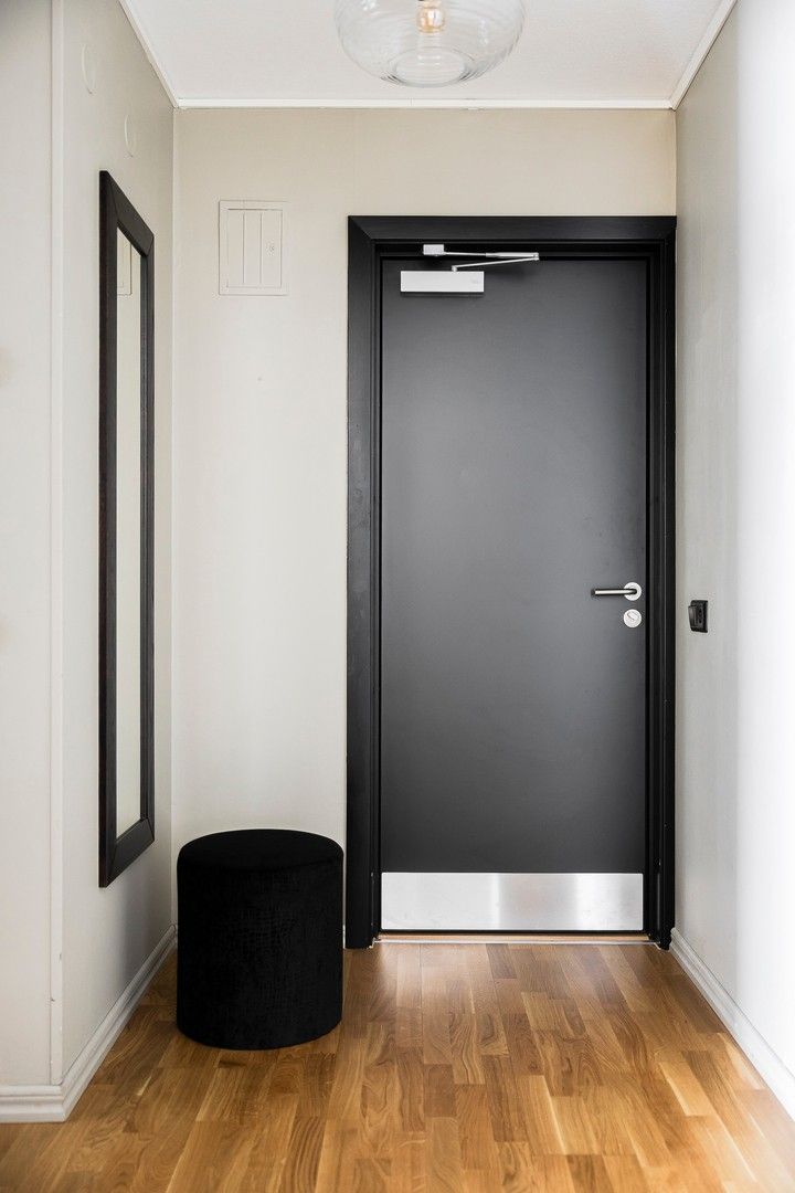 A hallway with a black door, a black cylindrical object, and a framed picture on the wall.