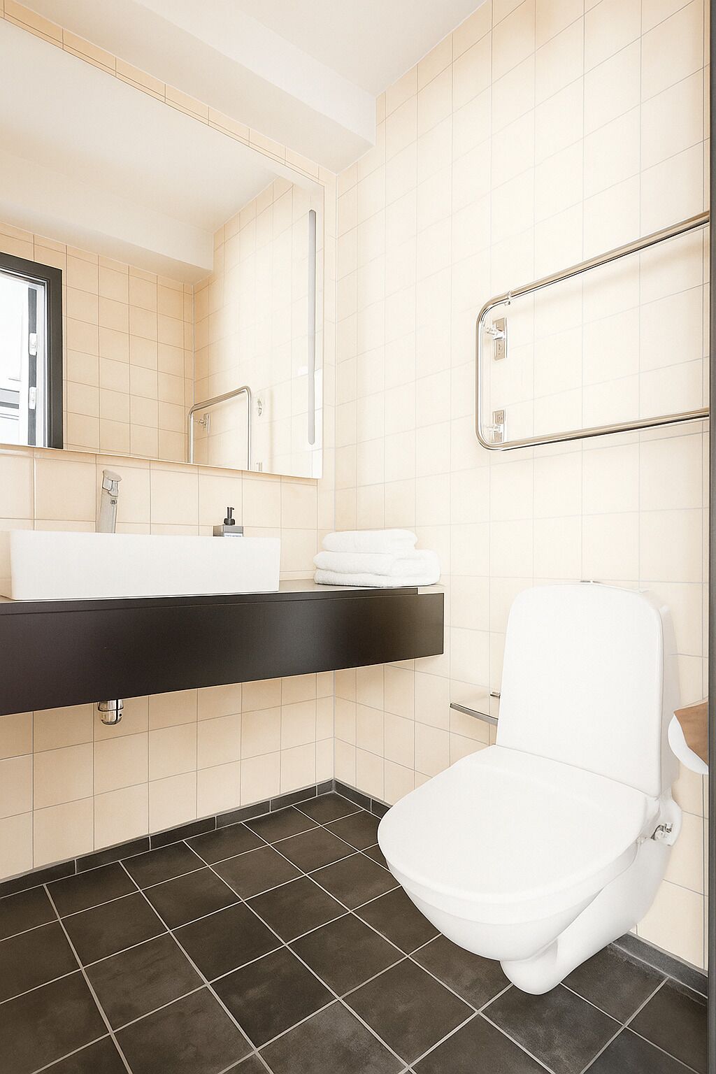 Un baño moderno con inodoro blanco, tocador negro, espejo y toallero.