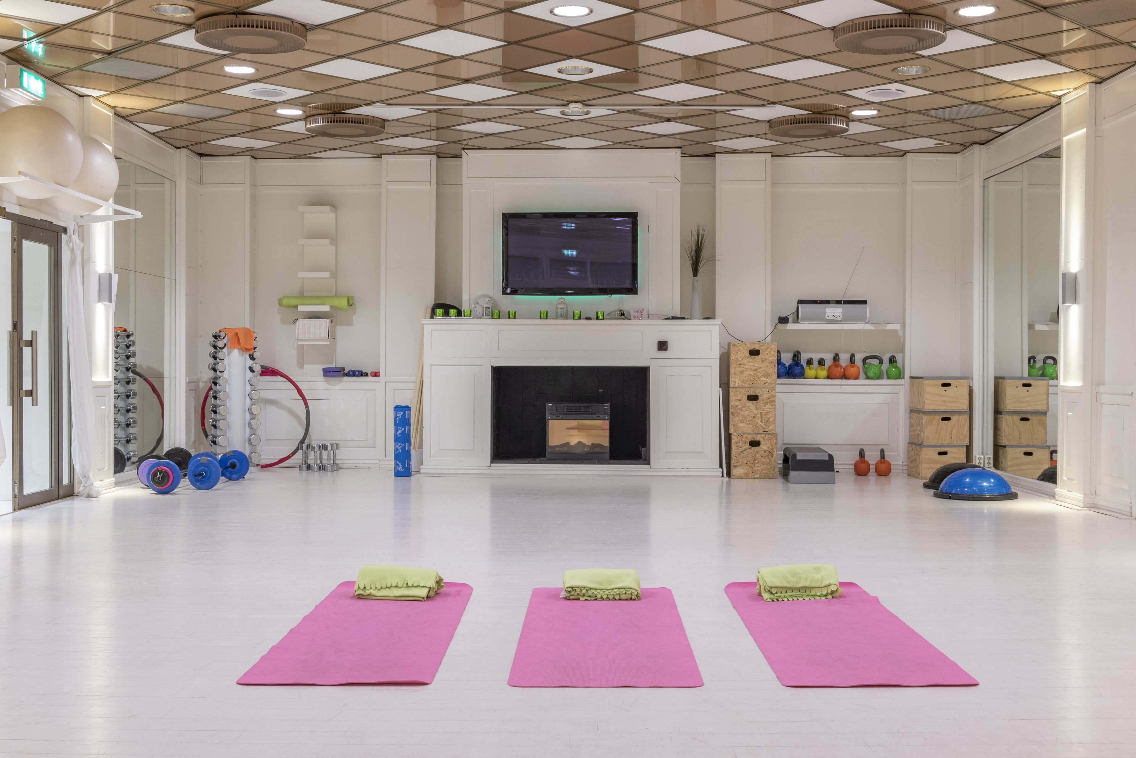 A spacious room with a large flat-screen TV mounted on the wall, a fireplace, and exercise mats on the floor.