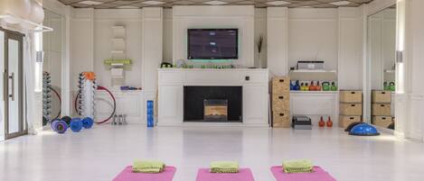 A spacious room with a large flat-screen TV mounted on the wall, a fireplace, and exercise mats on the floor.