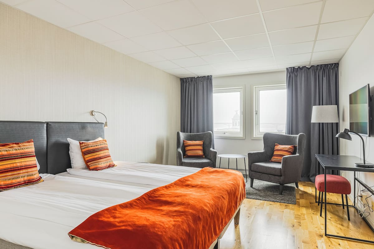 Une chambre d’hôtel avec un grand lit, deux fauteuils, un bureau et une télévision.