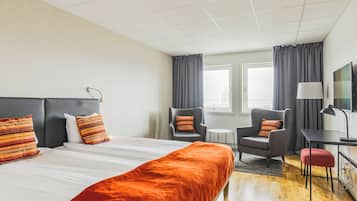 Ein Hotelzimmer mit einem großen Bett, zwei Sesseln, einem Schreibtisch und einem Fernseher.