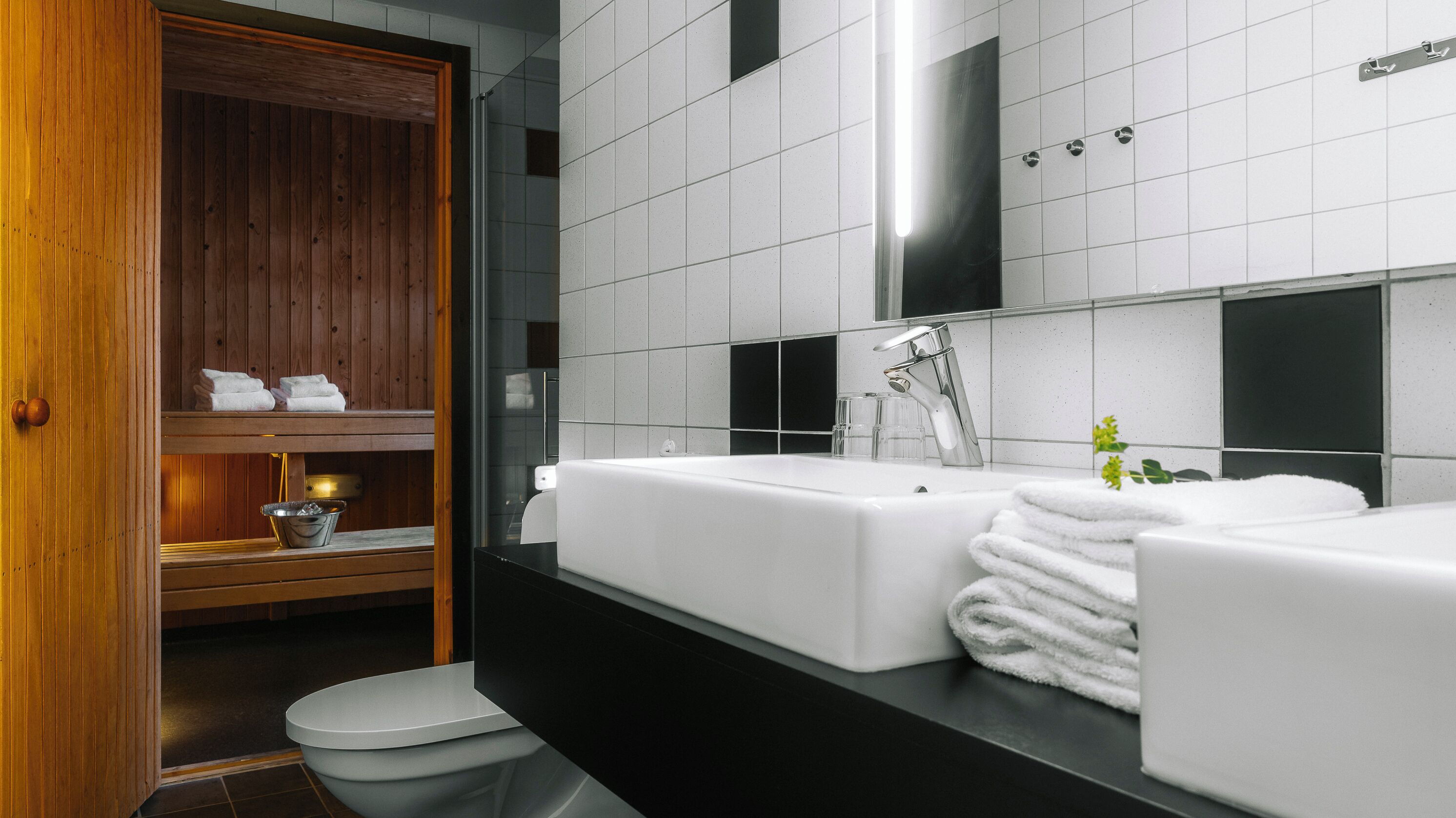 A modern bathroom with a wooden vanity, a large mirror, and a separate toilet area.