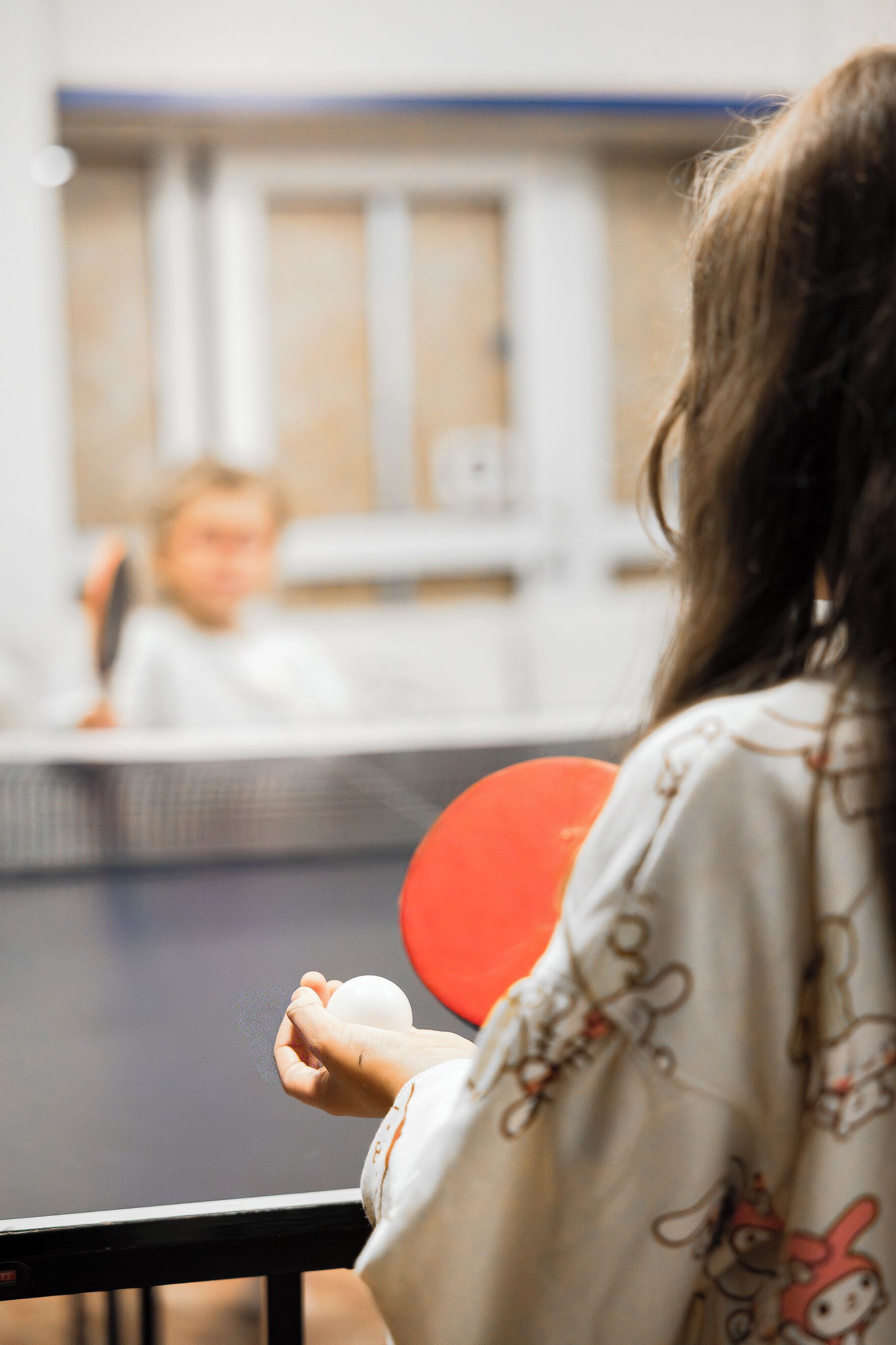 Una persona juega al tenis de mesa en un espacio interior usando una paleta roja.
