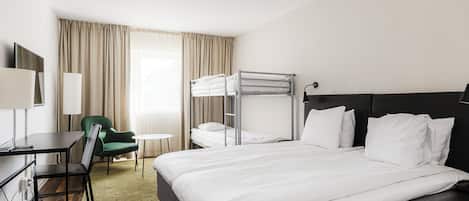 Habitación de hotel con una litera, un escritorio con silla, una mesita redonda y un sillón verde.