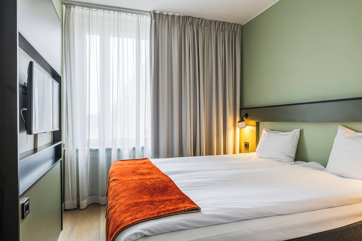 Une chambre d’hôtel avec un lit, des rideaux, une télévision et une lampe fixée au mur.