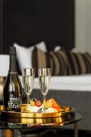 A bottle of Prosecco, two glasses, and a tray with food and flowers on a table in a hotel room.