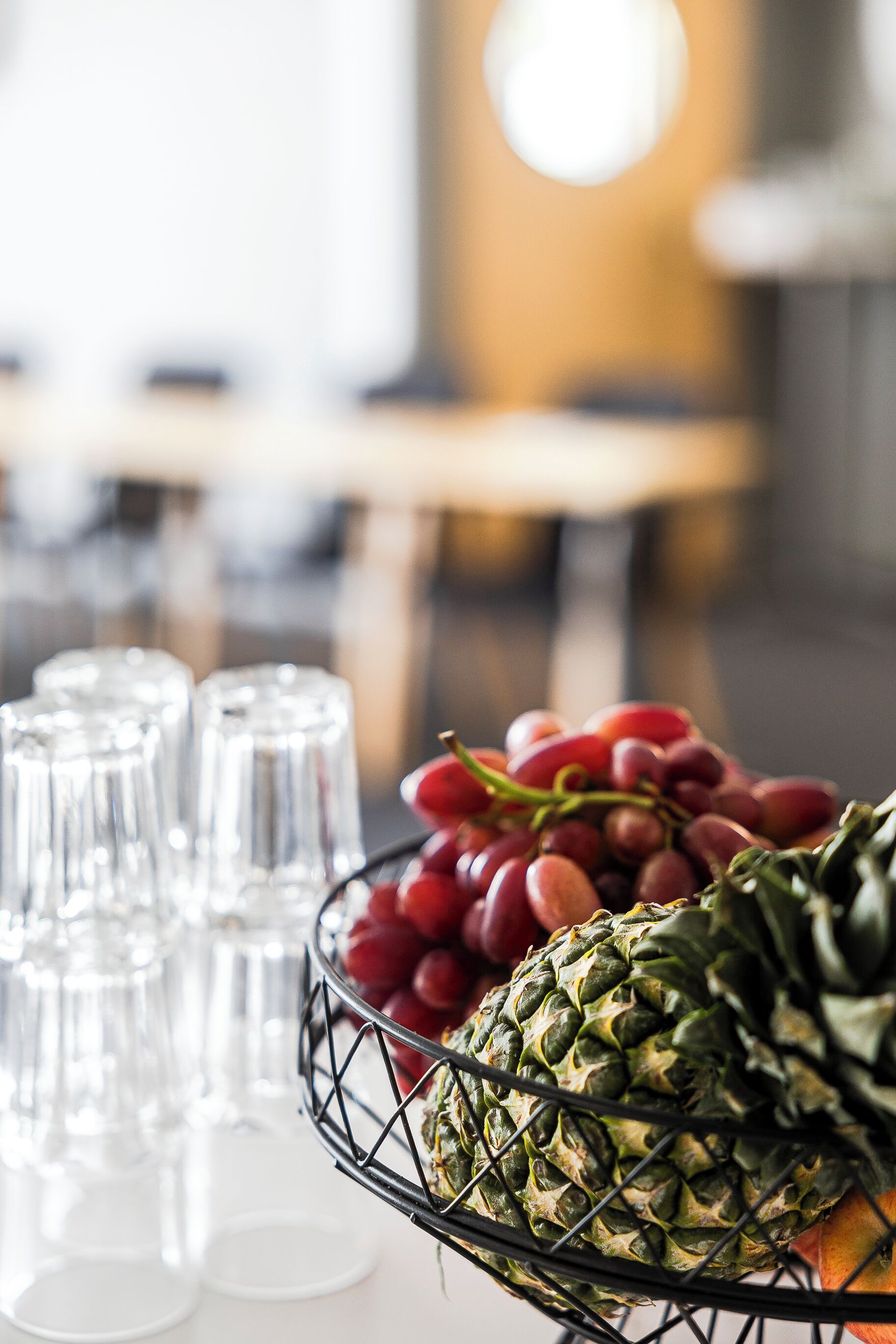 A table with a fruit basket containing grapes and a pineapple, and several empty glasses.