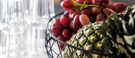 A table with a fruit basket containing grapes and a pineapple, and several empty glasses.