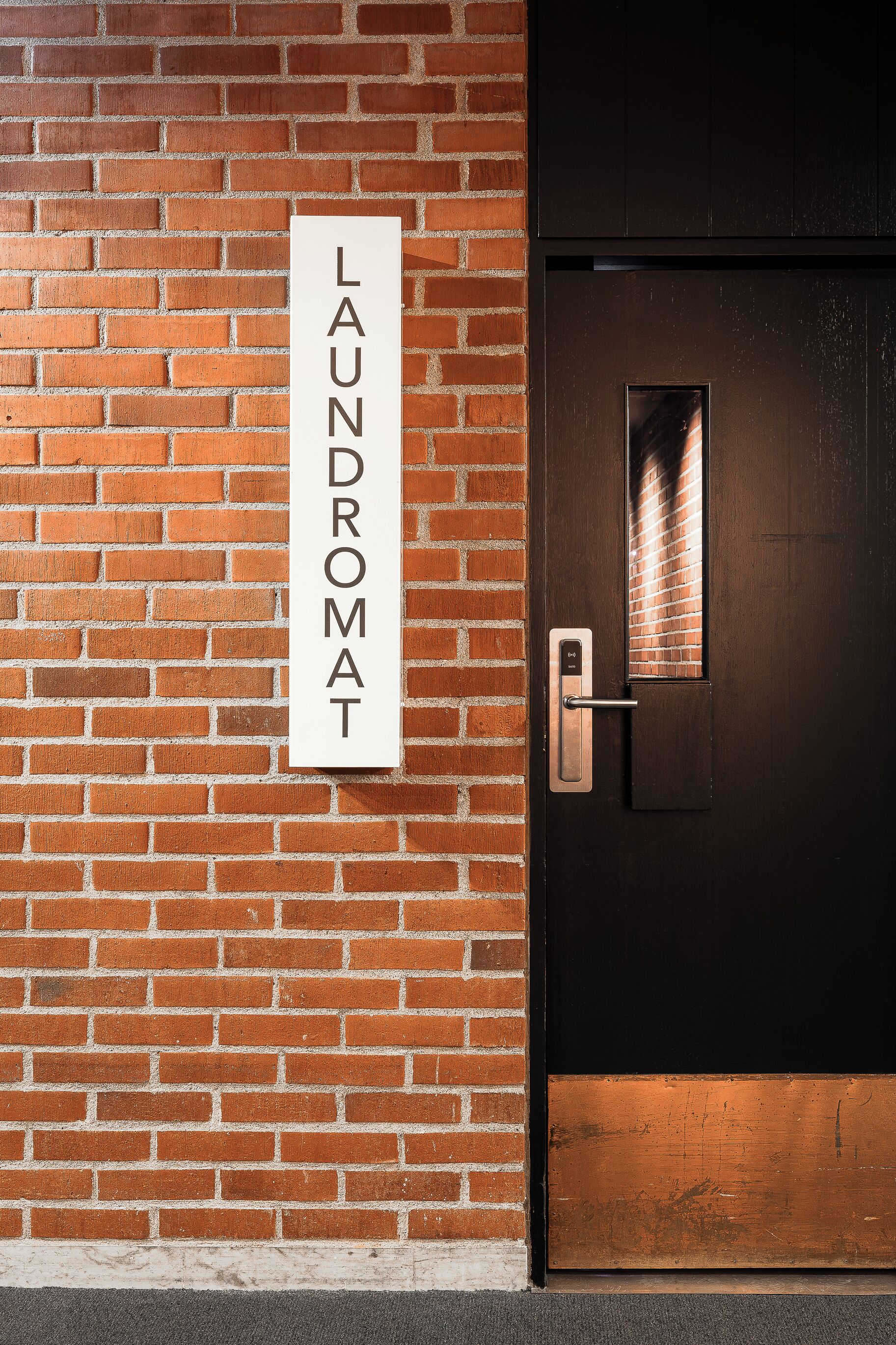 Un muro in mattoni con un cartello che riporta la scritta “LAUNDROMAT” e una porta con maniglia in metallo e una piccola finestra.