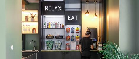 A self-service beverage station with a menu and snacks, a sink, and a potted plant.