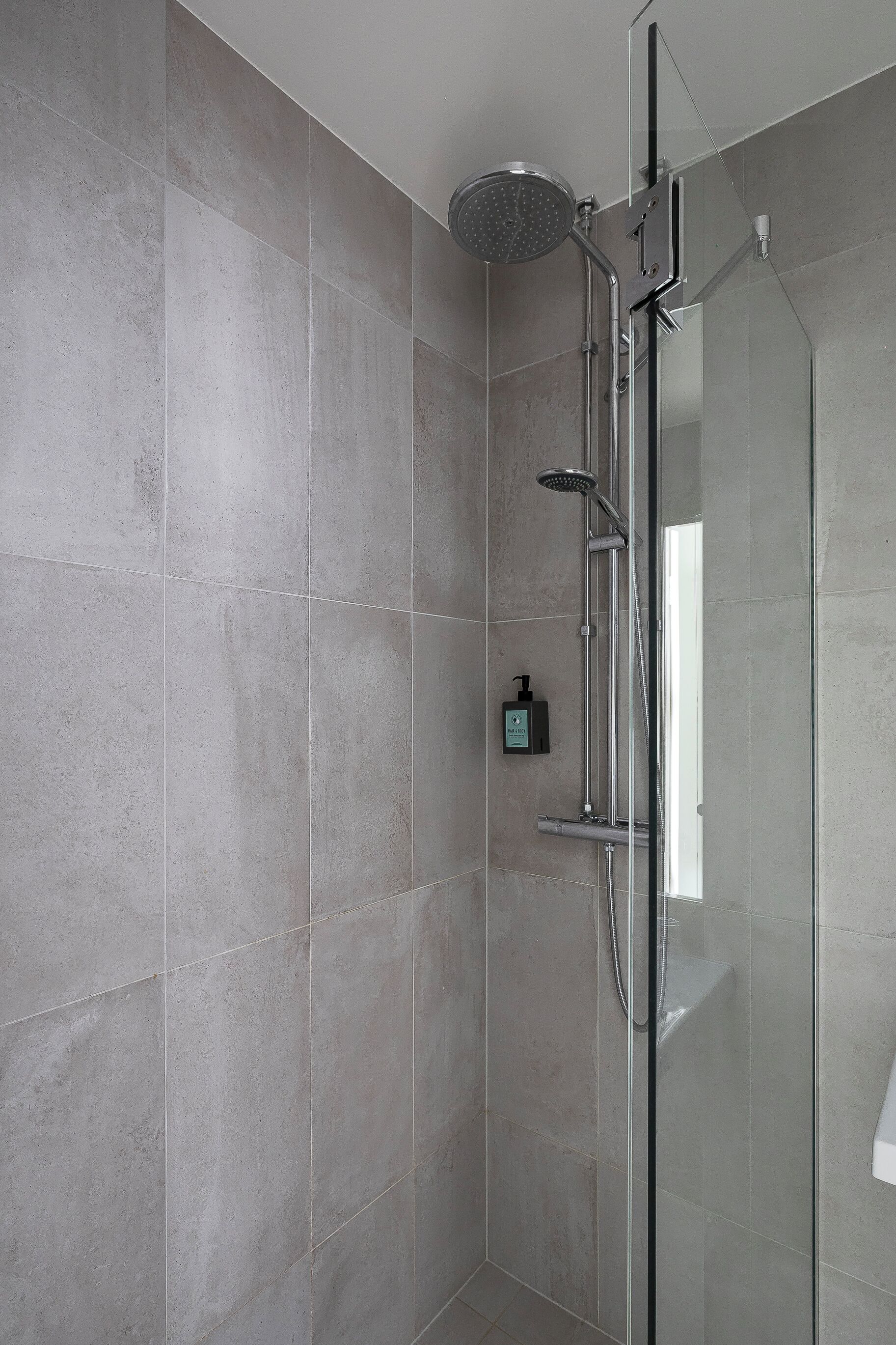 A modern shower with a glass enclosure, a handheld showerhead, and a wall-mounted control panel.
