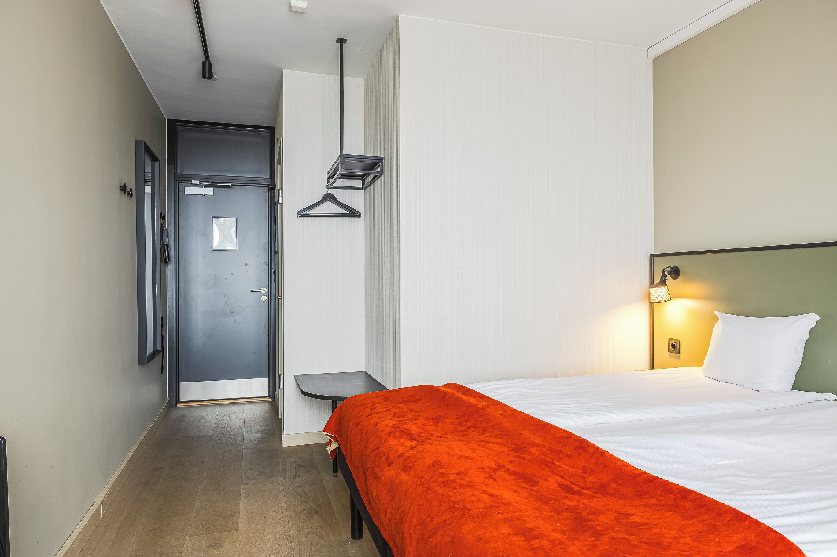 Ein Hotelzimmer mit einem Bett, einem Nachttisch, einer Hängelampe und einer Tür.