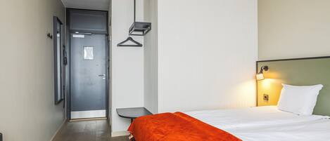 Ein Hotelzimmer mit einem Bett, einem Nachttisch, einer Hängelampe und einer Tür.
