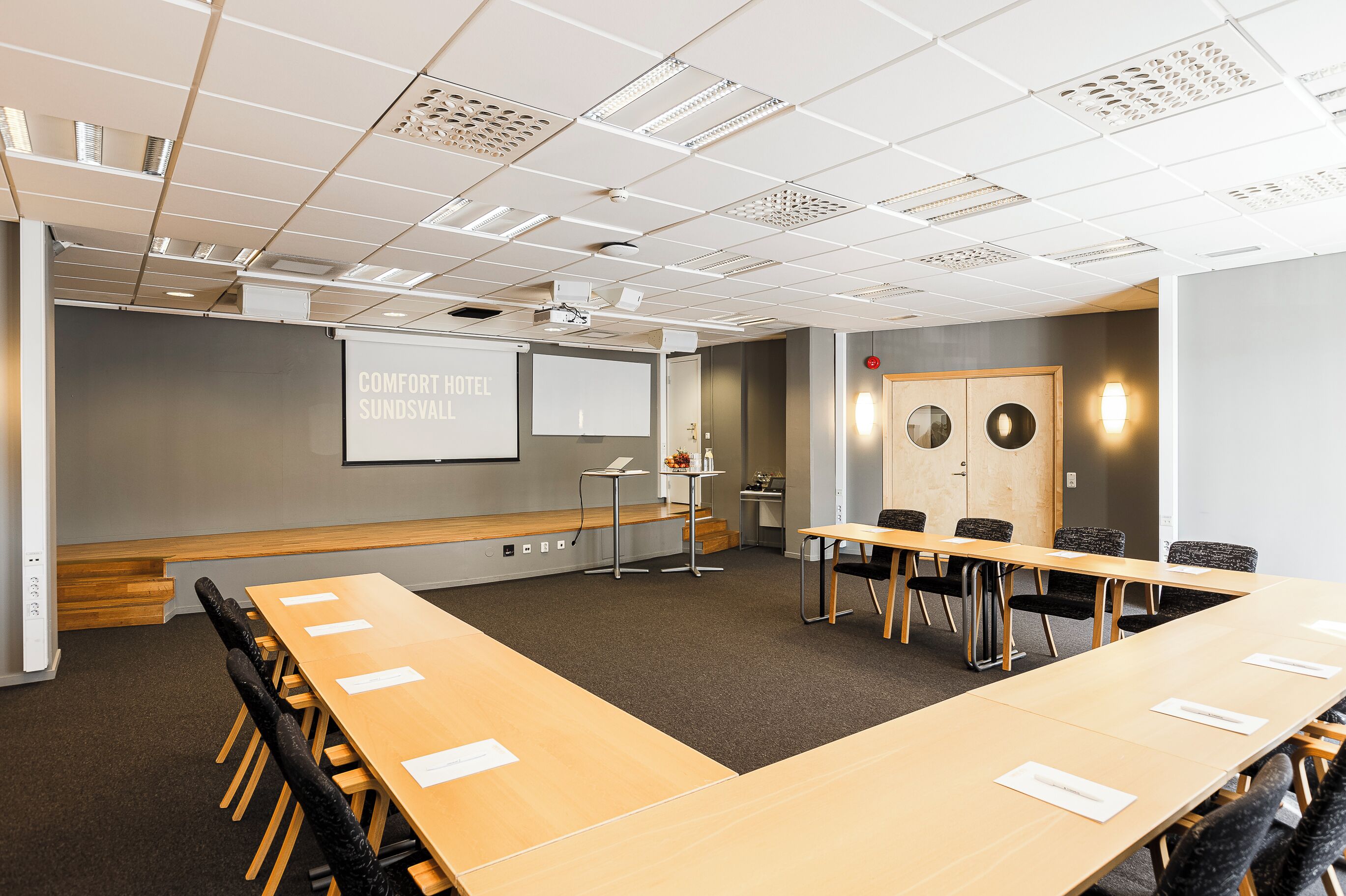 Ett konferensrum med ett långt bord, stolar, en projektorduk och en whiteboard.
