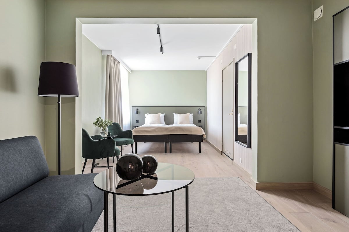 Une chambre d’hôtel moderne équipée d’un lit, d’un canapé, d’une table basse en verre et d’un bureau avec une lampe.