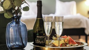Ett bord med en flaska prosecco, två glas, en tallrik med frukt och en vas med gröna blad.