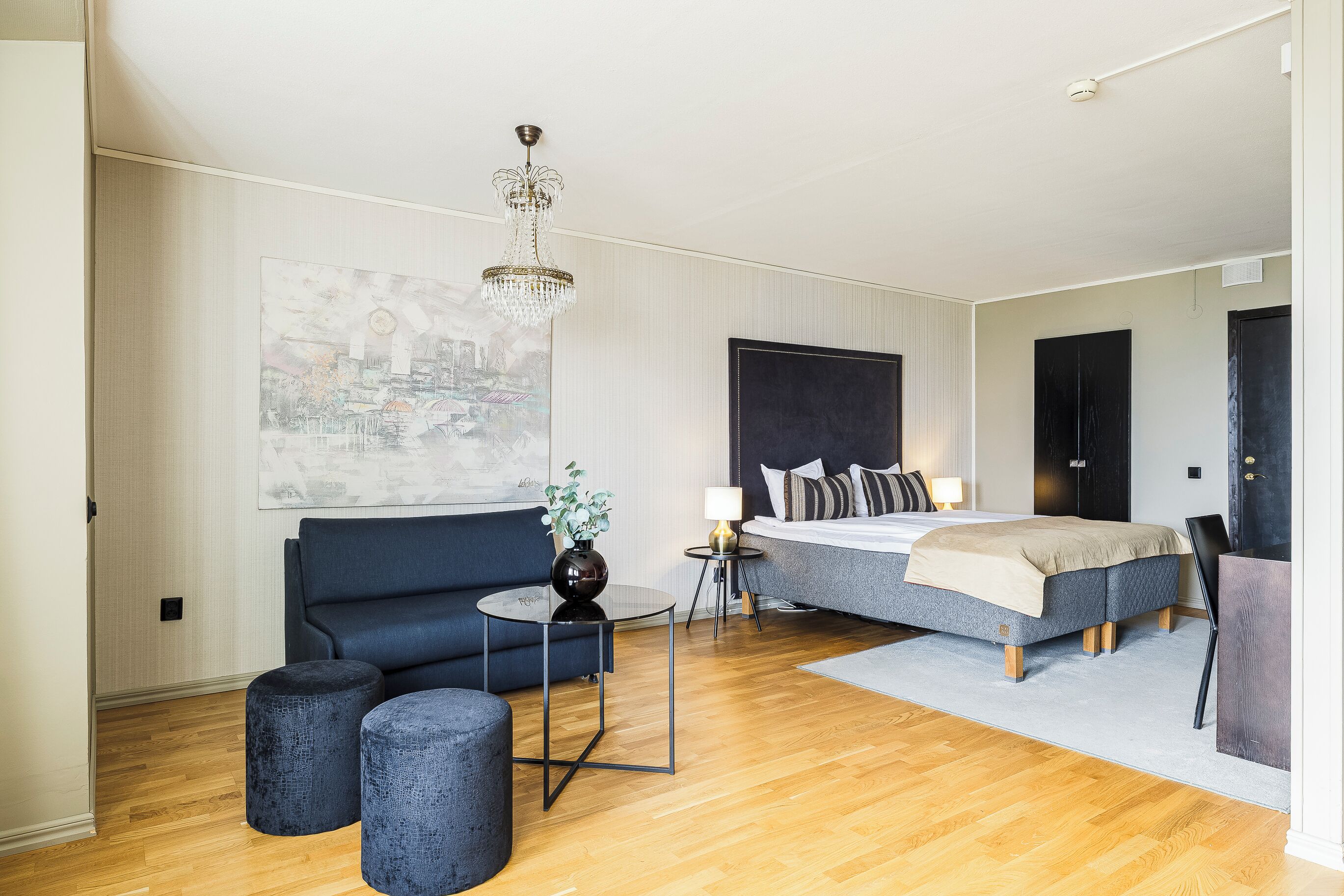 Una habitación de hotel moderna con una cama grande, un sofá, una mesita y un candelabro decorativo.