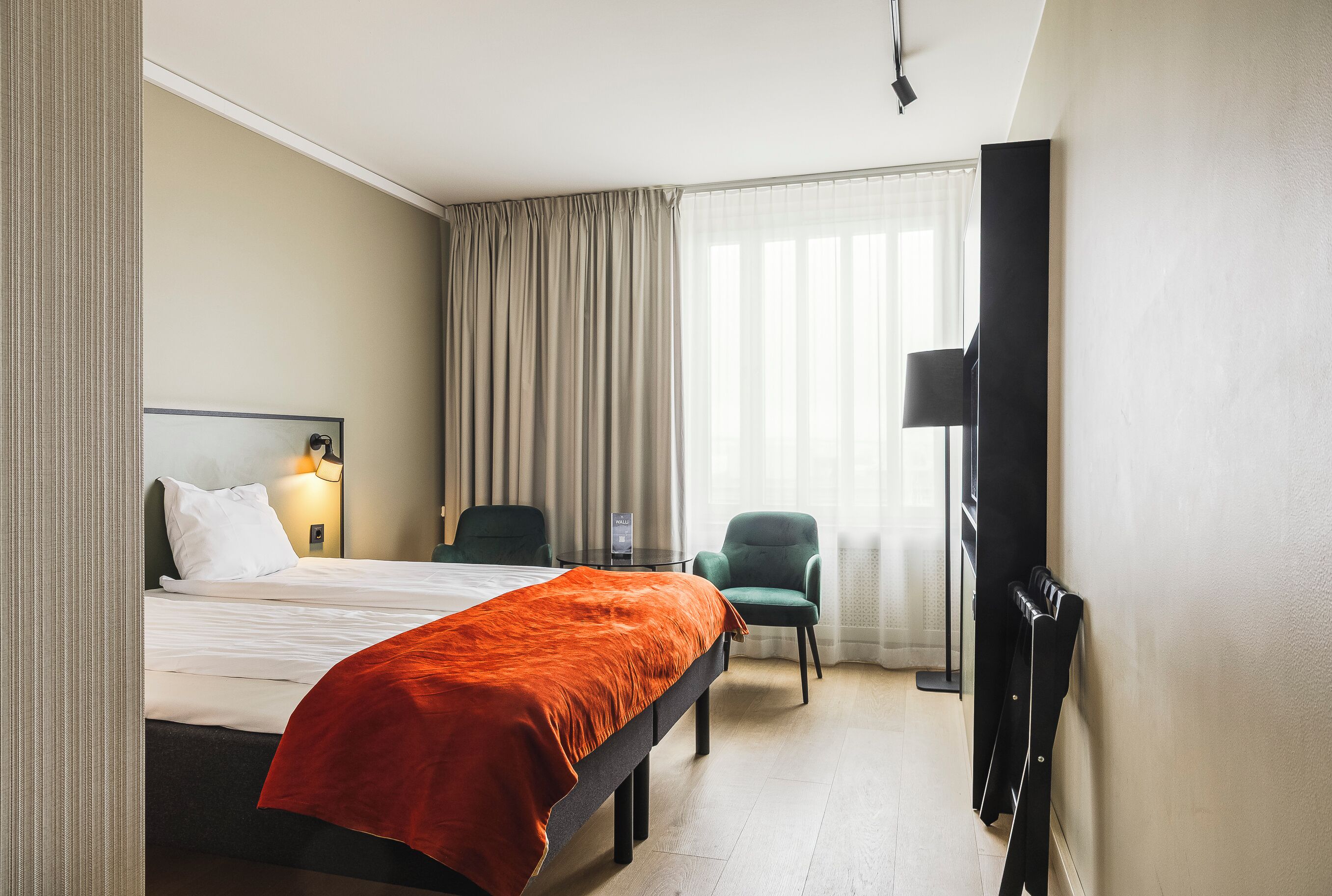 Una habitación de hotel con cama, escritorio, silla, televisor y ventana con cortinas.